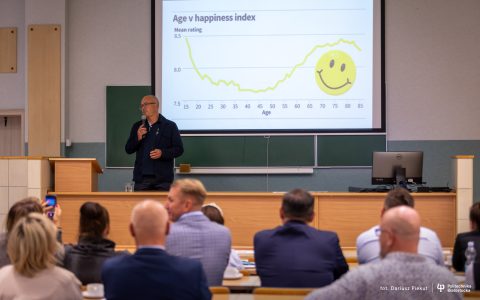 wykładowca na tle ekranu z uśmiechnięta buźką w auli